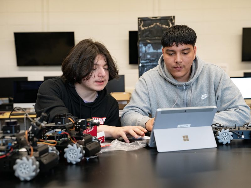 Students working at a laptop with drones on the desk in front of them.