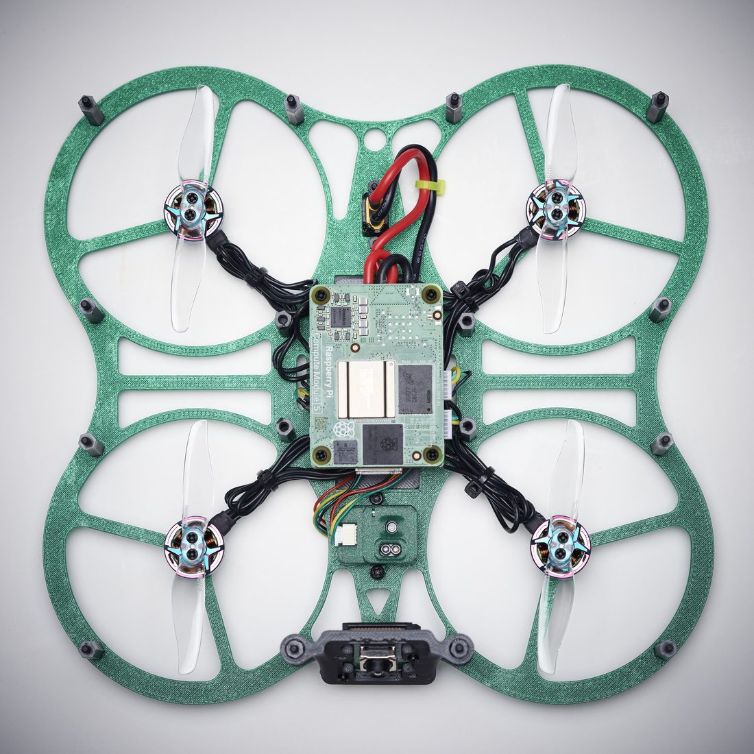 The same underside with the center cover removed, showing the Raspberry Pi compute module, the red and black power harness, and the motor leads routed through the frame.