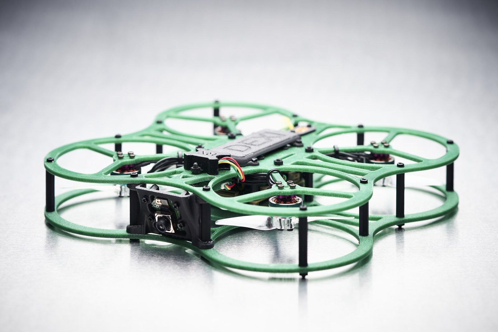 A green ducted DEXI-3 on a studio sweep, seen from three quarters, with the forward camera module and the electronics mounted on top of the frame.