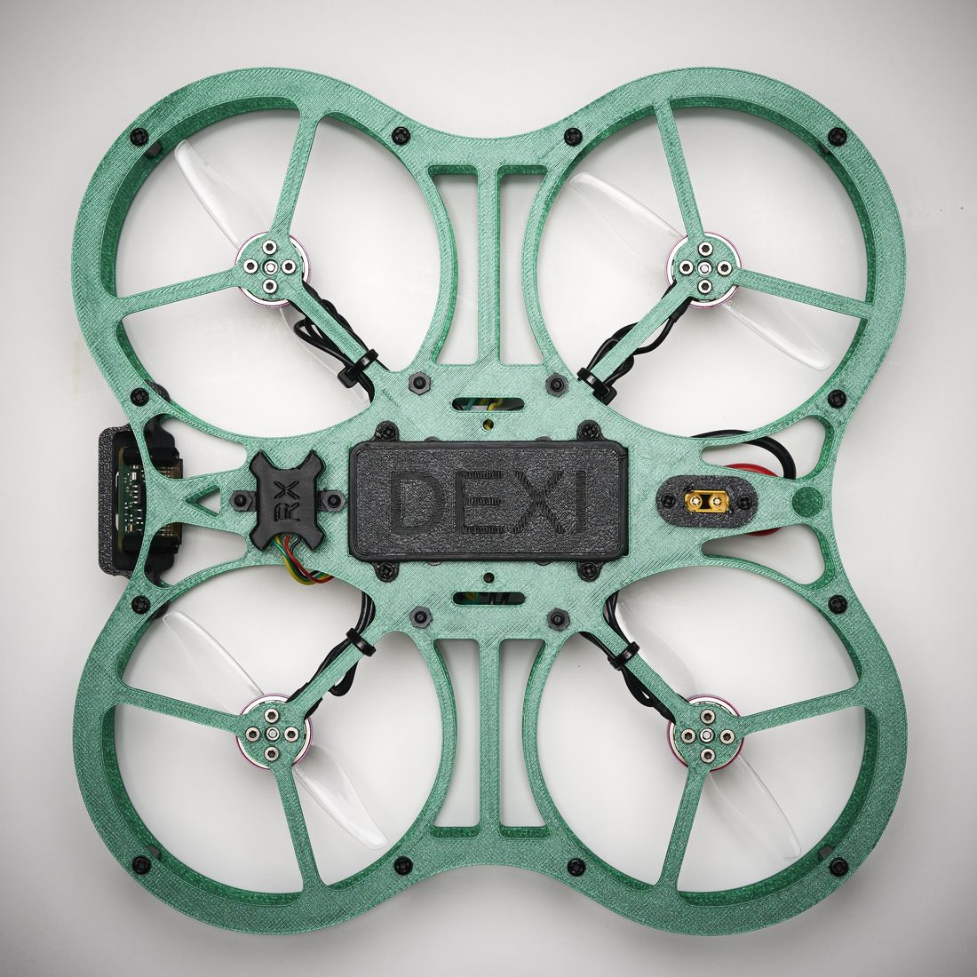 A DEXI-3 photographed from directly above: green ducted frame, four motors with propellers, a black battery plate marked DEXI, and the XT60 power connector.