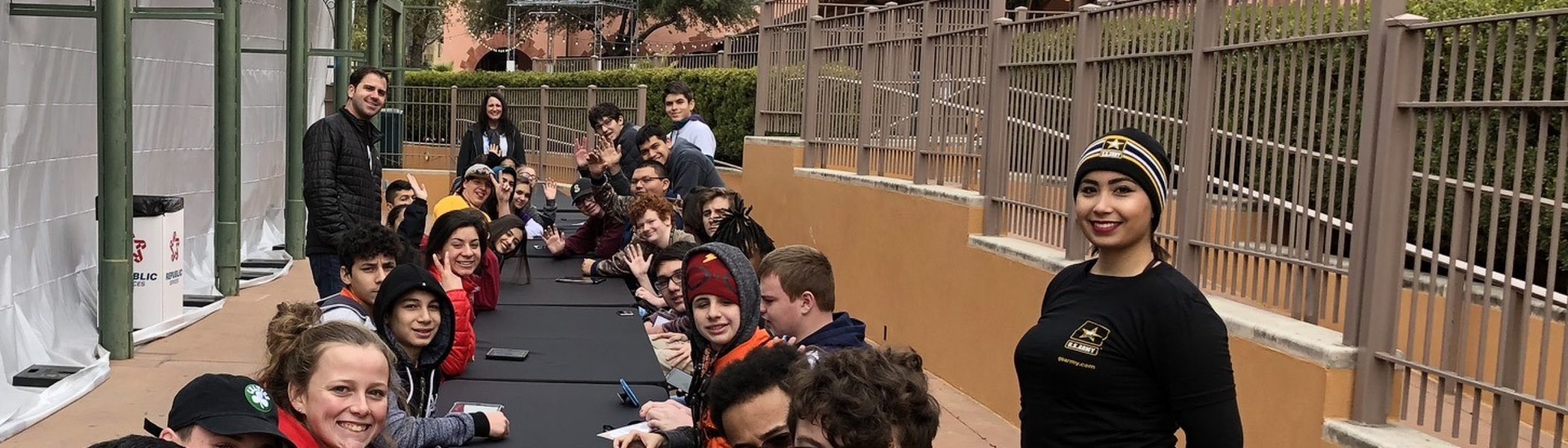 A long table of students seated with small drones in front of them at a school event.