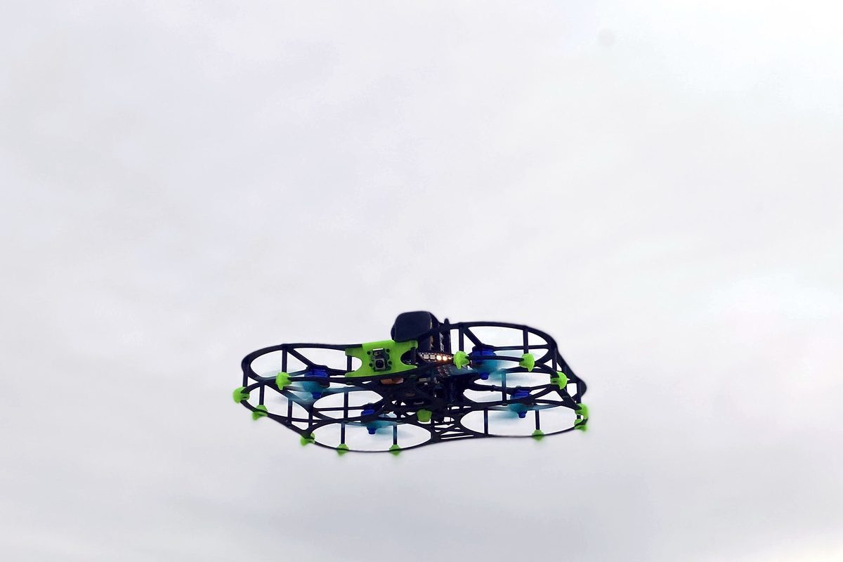A caged DEXI drone hovering against an overcast sky.