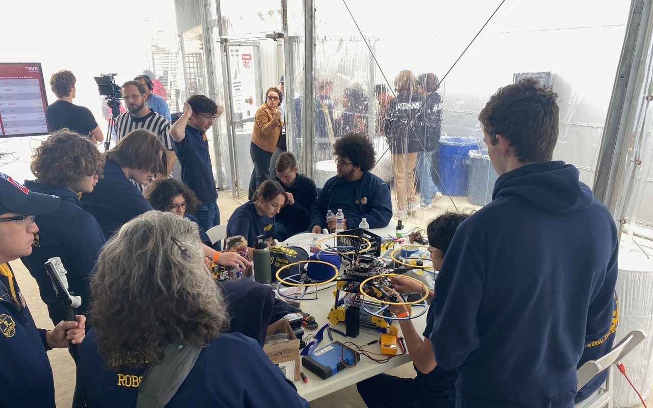 Students working on drones at long tables in a competition pit.